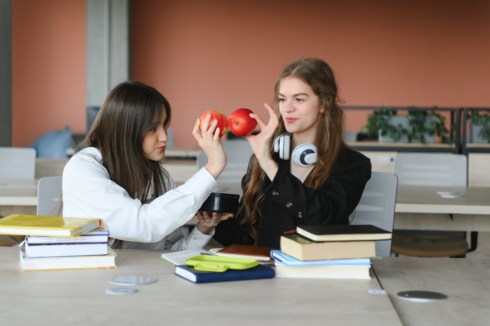 Two fifteen-year-old schoolgirls reading books and taking abstract in copybooks are doing homework in the school library